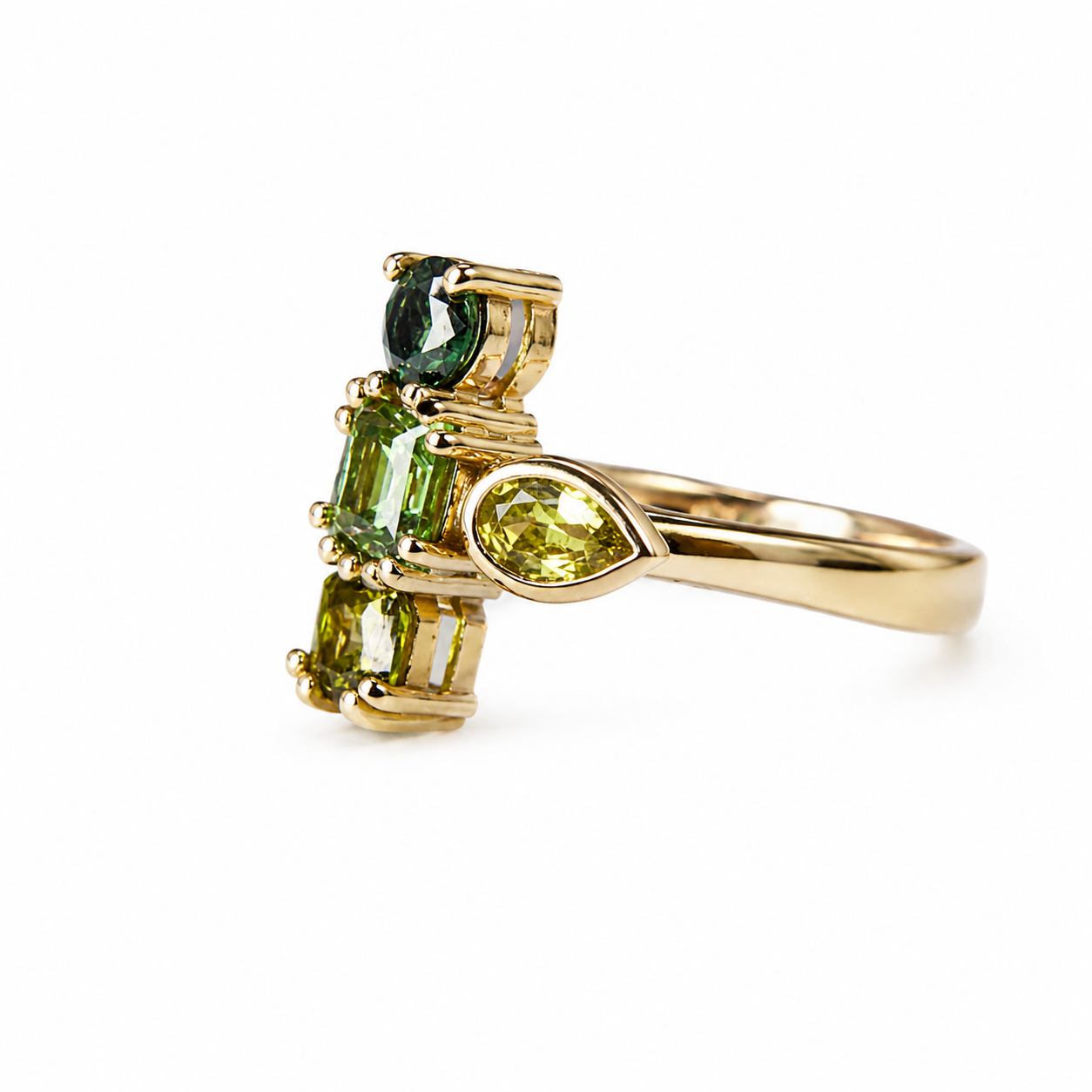 A yellow gold ring featuring a cluster of green gemstones, including a marquise-cut lime green stone, a rectangular emerald-cut green stone, and a round dark green stone, set on a polished gold band against a white background.