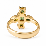 A gold ring with a decorative top featuring green gemstones, shown on a plain white background.