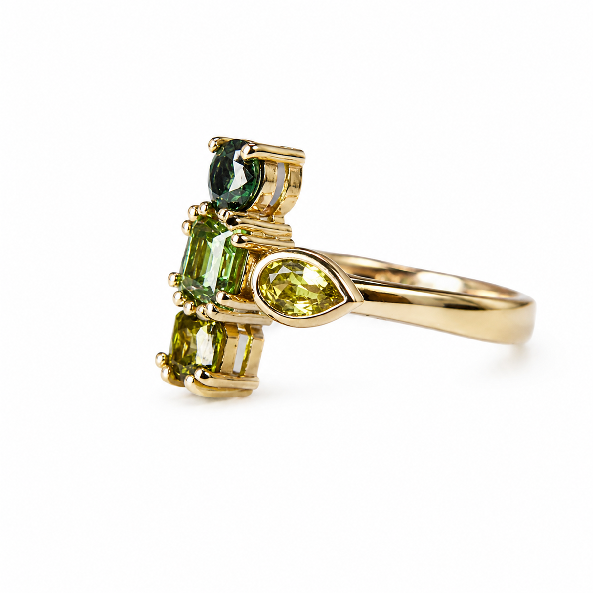 A yellow gold ring featuring a cluster of green gemstones, including a marquise-cut lime green stone, a rectangular emerald-cut green stone, and a round dark green stone, set on a polished gold band against a white background.