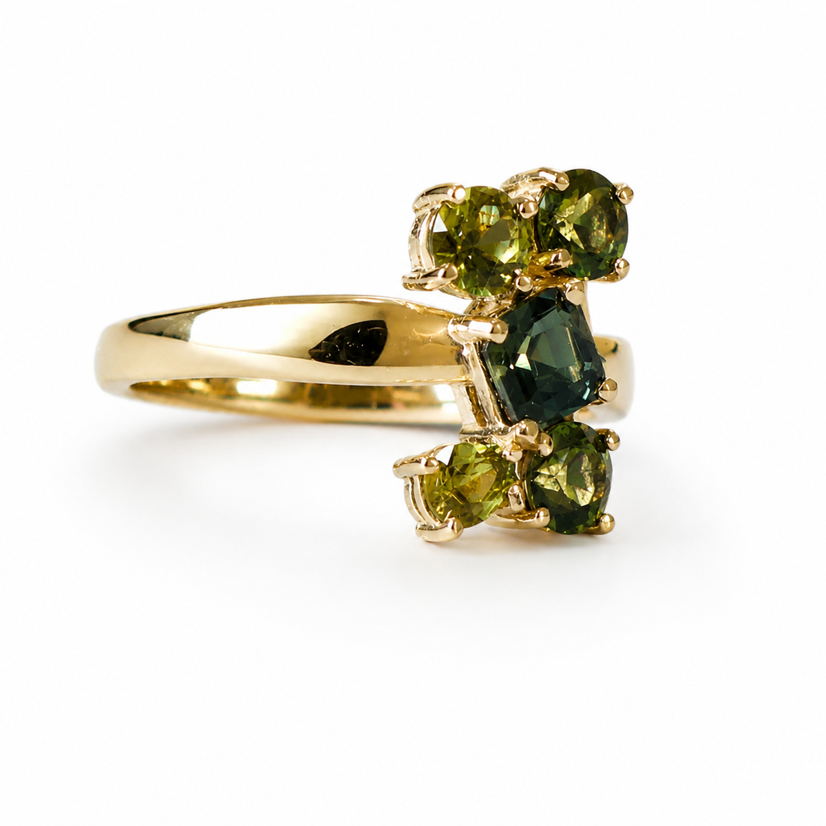 A yellow gold ring featuring a cluster of green gemstones, including a central marquise-cut dark green stone and three oval green stones on either side, set against a plain white background.