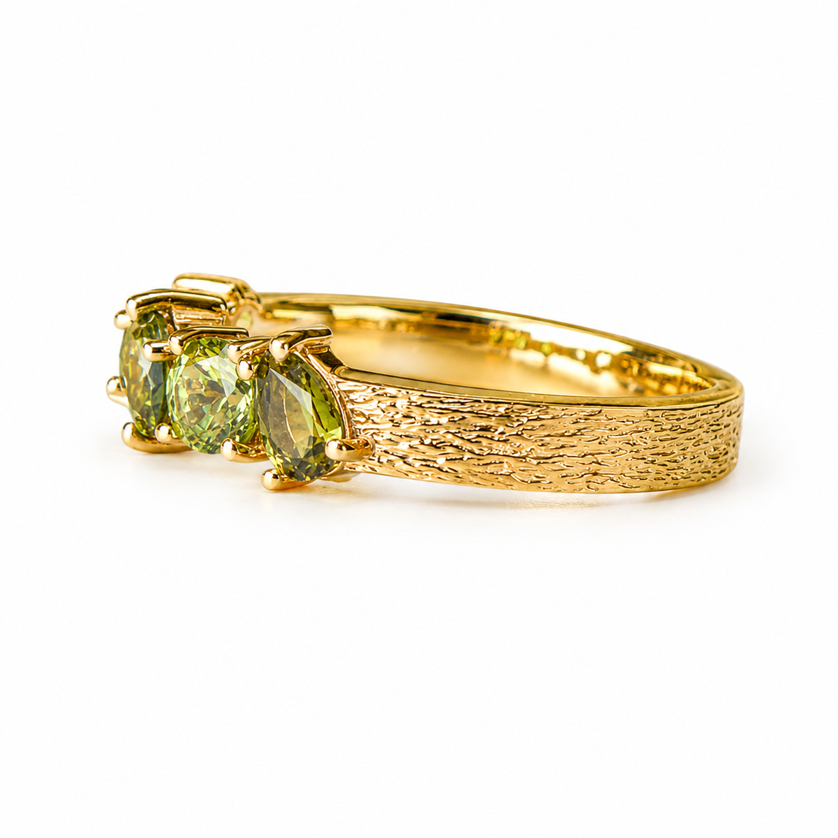 A gold ring featuring three marquise-cut green gemstones in a textured tree-bark style band, shown on a plain white background.