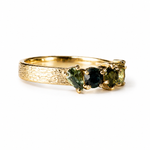 A gold ring featuring three marquise-cut green gemstones in a textured tree-bark style band, shown on a plain white background.