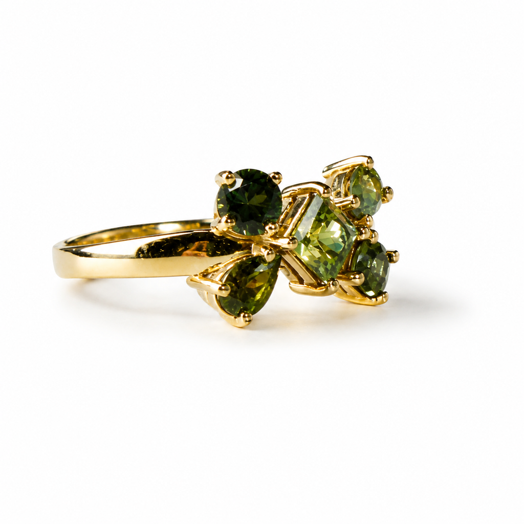 A gold ring featuring a cluster of green gemstones, including a round center stone and three pear-shaped side stones, set against a plain white background.