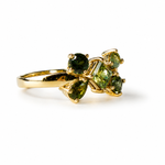 A gold ring featuring a cluster of green gemstones, including a round center stone and three pear-shaped side stones, set against a plain white background.