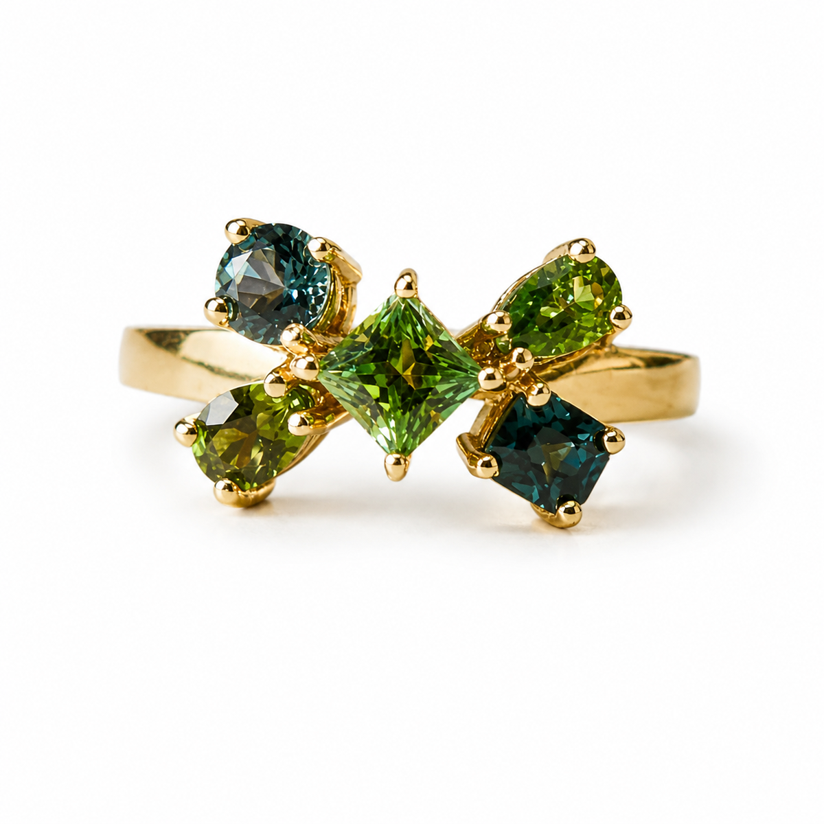 A gold ring featuring a bow-like cluster of green gemstones, including a central square-cut green stone and four surrounding round-cut green and blue-green stones, set against a plain white background.