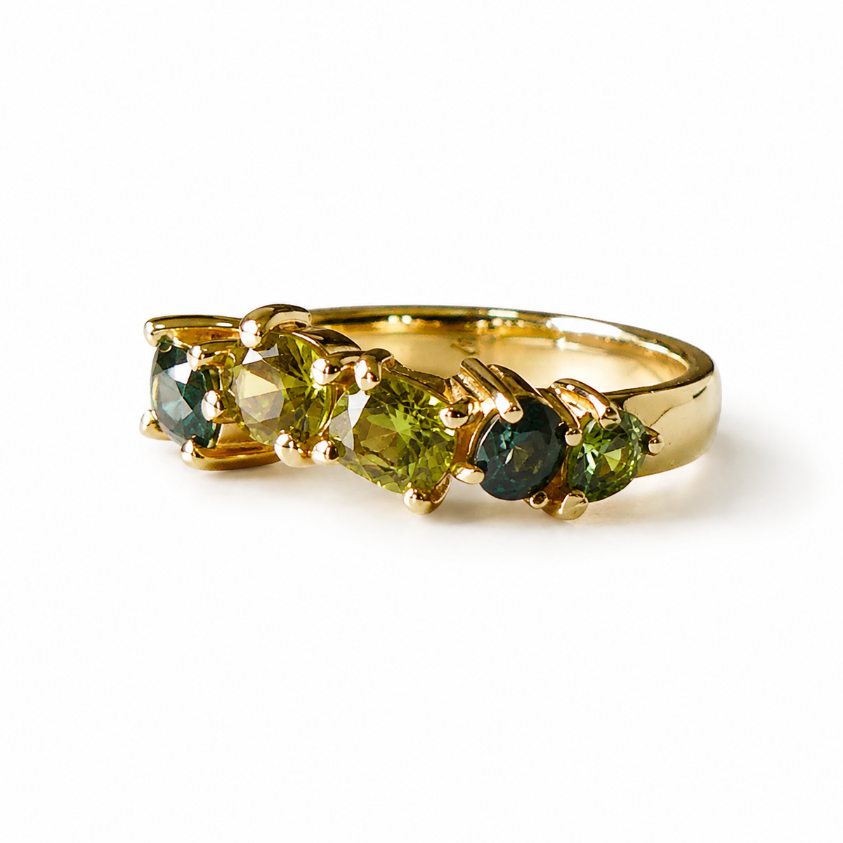 A gold ring featuring a row of faceted green gemstones in a prong setting, photographed on a clean white background.