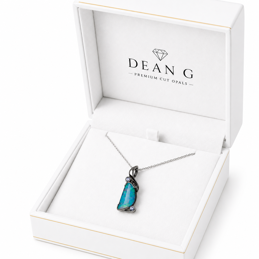 A DEANG brand necklace with a vibrant blue-green opal pendant in a silver setting, presented inside an open white jewelry box.
