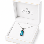 A DEANG brand necklace with a vibrant blue-green opal pendant in a silver setting, presented inside an open white jewelry box.