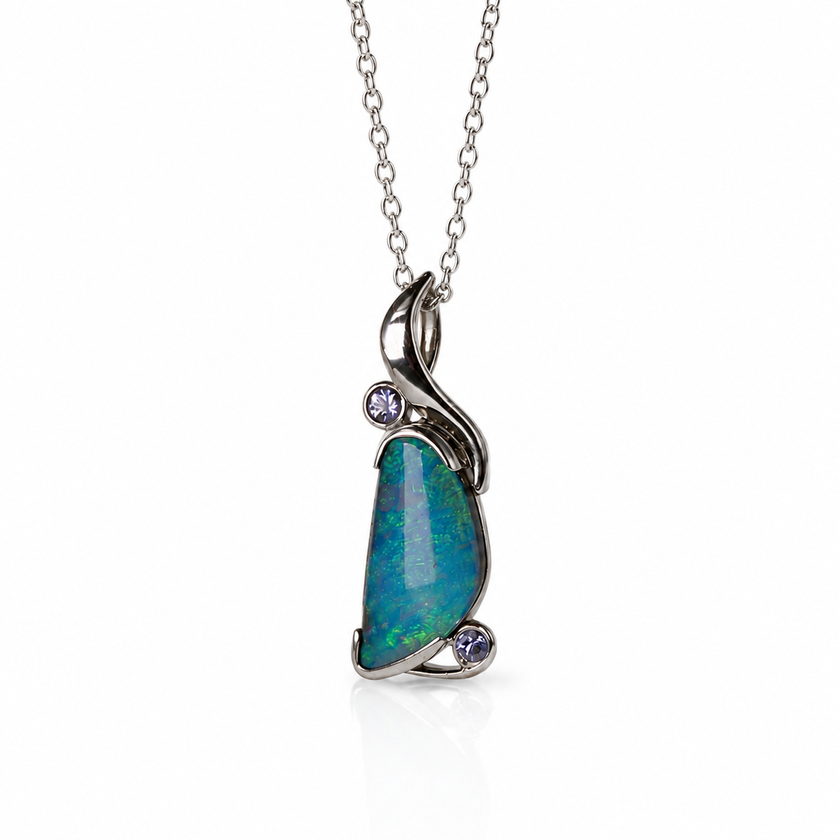 A silver pendant necklace featuring a teardrop-shaped blue-green opal stone with two small round purple gemstones, suspended from a delicate silver chain on a white background.