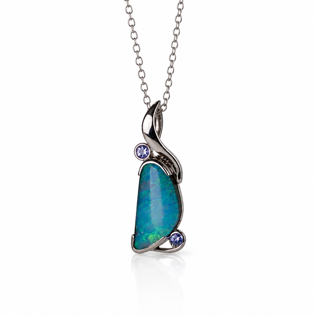 A silver pendant necklace featuring a teardrop-shaped blue-green opal stone with two small round purple gemstones set in a polished silver bail, suspended from a delicate silver chain on a white background.