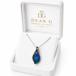 A teardrop-shaped cut opal pendant necklace with a dark metal setting, displayed inside an open white Dean G Premium Cut Opals gift box.