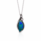 A silver pendant necklace featuring a teardrop-shaped opal stone with vibrant blue and green play-of-color, accented by a small clear round stone and tiny pavé-set stones along the edge, suspended from a delicate silver chain on a white background.
