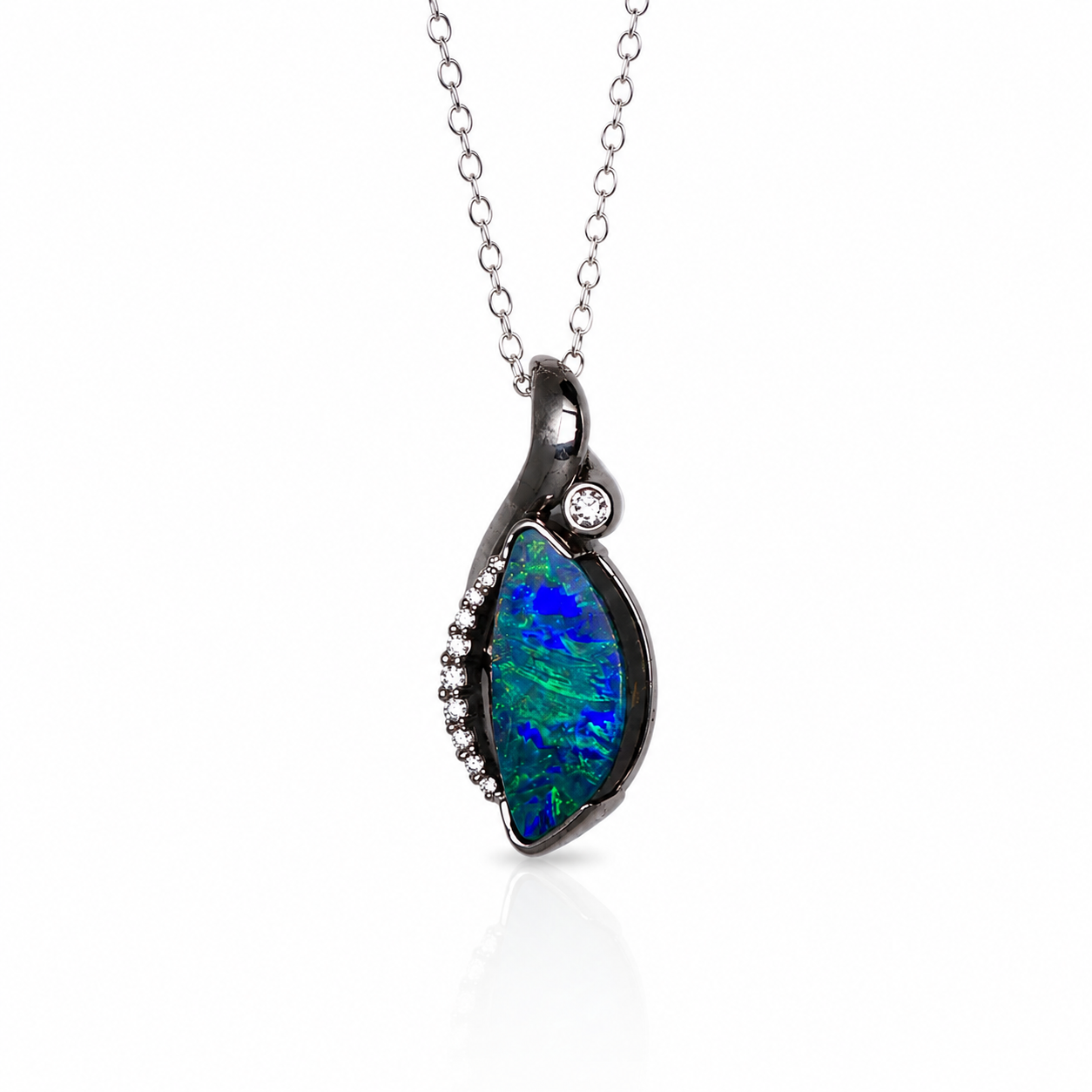 A silver pendant necklace featuring a teardrop-shaped opal stone with vibrant blue and green play-of-color, accented with a small clear round gemstone and a row of tiny clear beads on a white background.