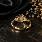Gold ring with a central gemstone on a dark surface with dried flowers.