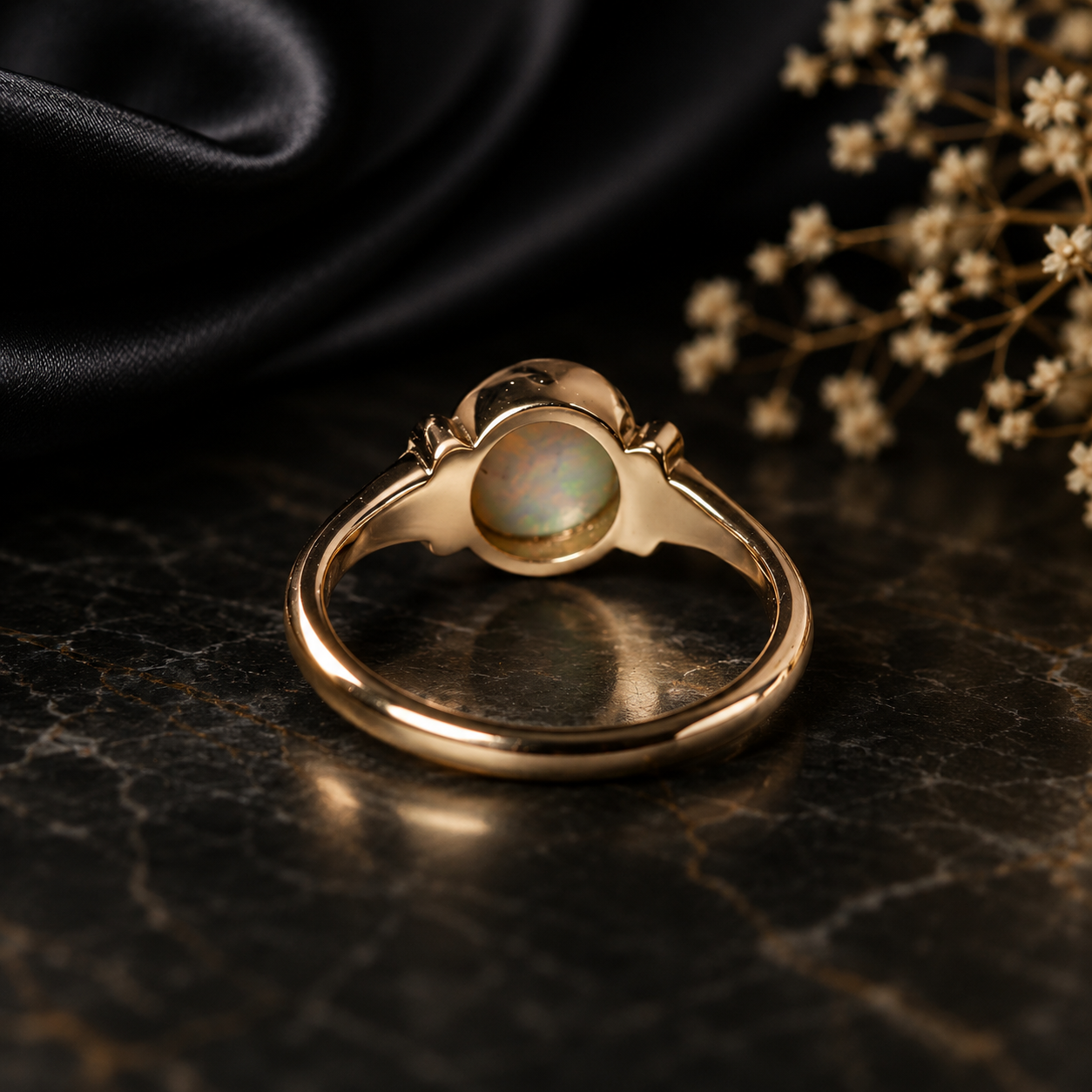 Gold ring with a central gemstone on a dark surface with dried flowers.