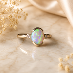 Gold ring with an opal stone on a marble surface with dried flowers.