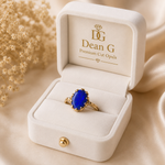 Gold ring with a blue gemstone in a Dean G jewelry box on a beige background