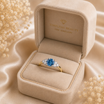 Gold ring with a blue gemstone in a 'Timeless Beauty' jewelry box on a beige fabric background.