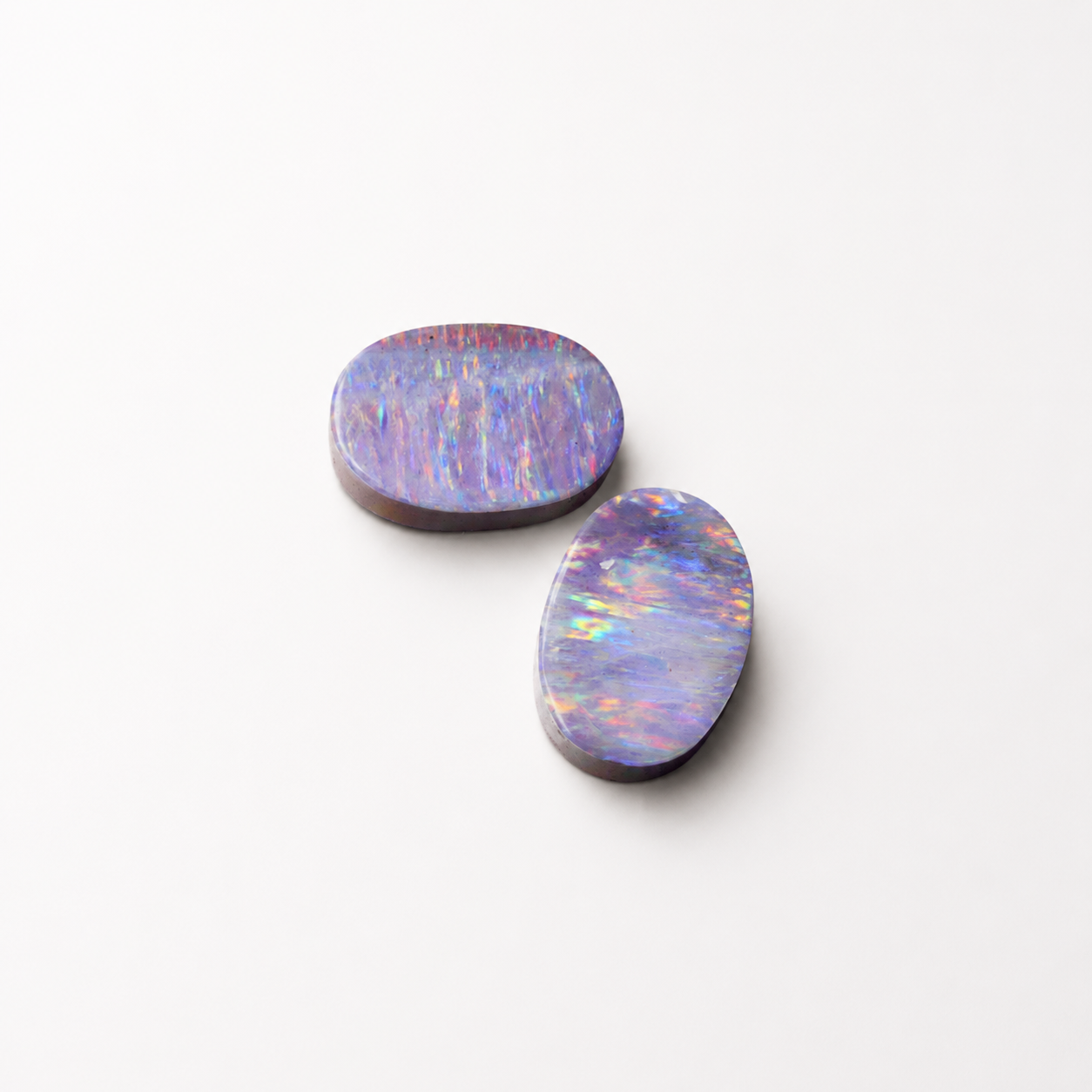 Two iridescent opal stones on a white background