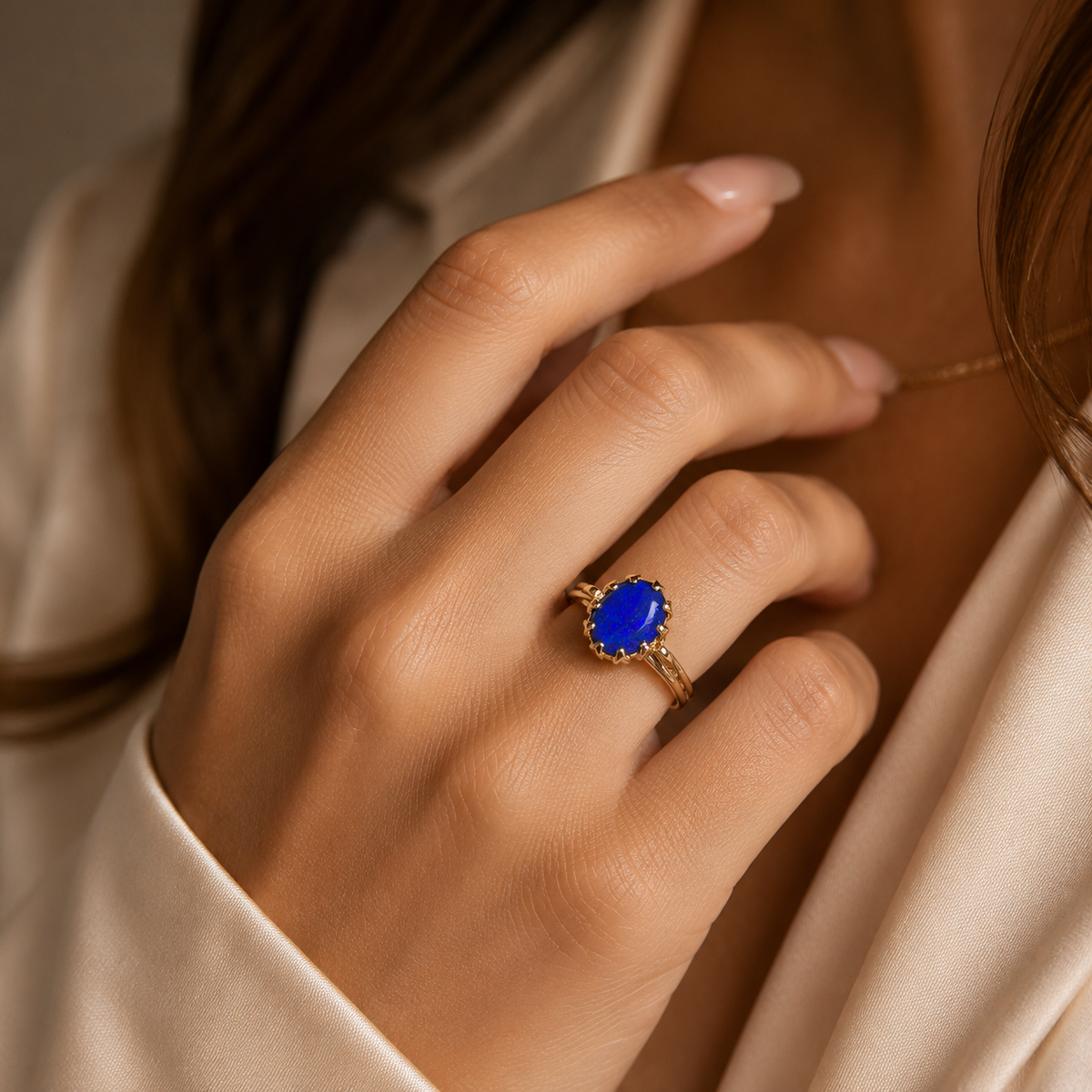 Hand wearing a ring with a blue gemstone against a neutral background