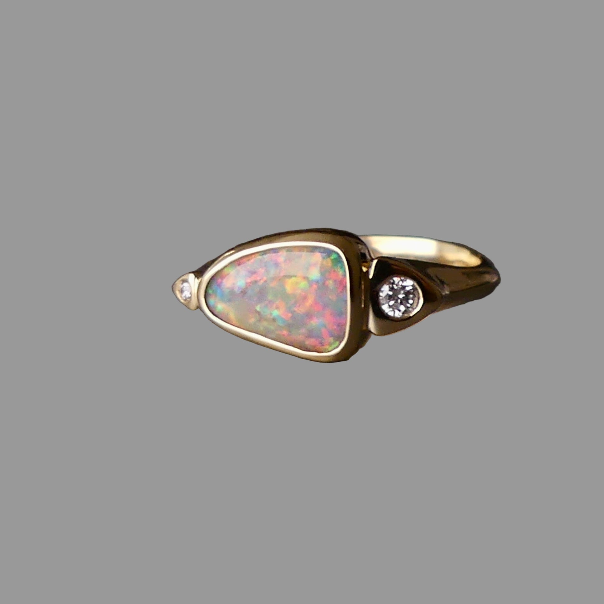 Gold ring with a colorful gemstone and diamond on a dark background