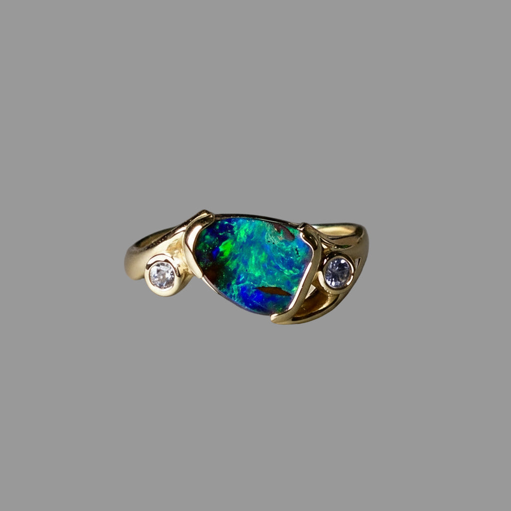 Gold ring with a colorful gemstone and small diamonds on a gray background