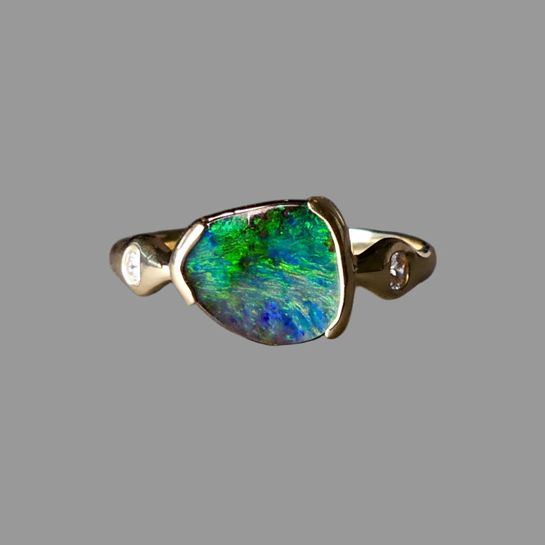 Gold ring with a large green and blue stone on a gray background