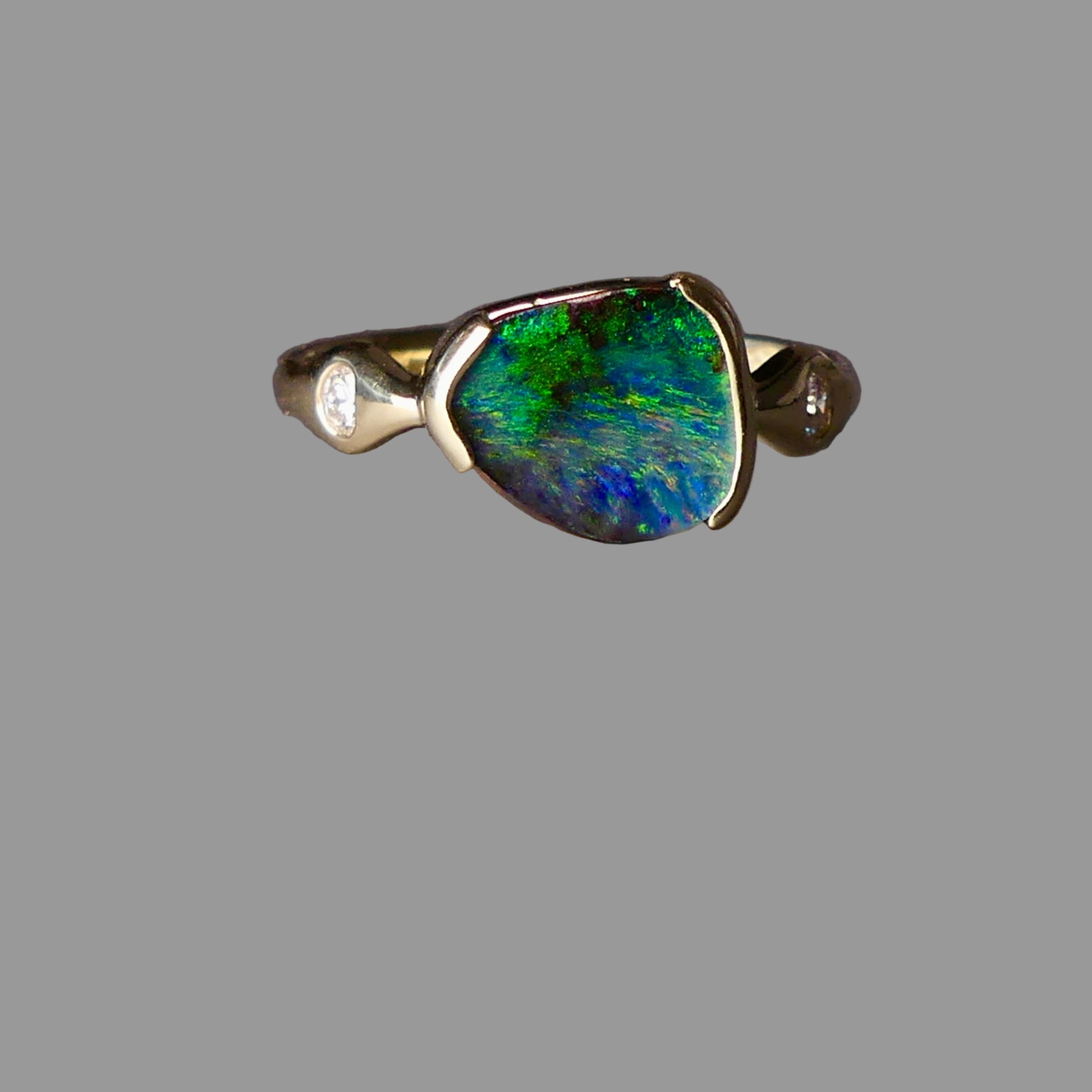 Gold ring with a green and blue gemstone on a gray background