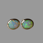Pair of opal stud earrings with gold setting on a dark background