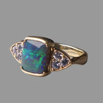 Gold ring with a colorful gemstone and smaller stones on a gray background