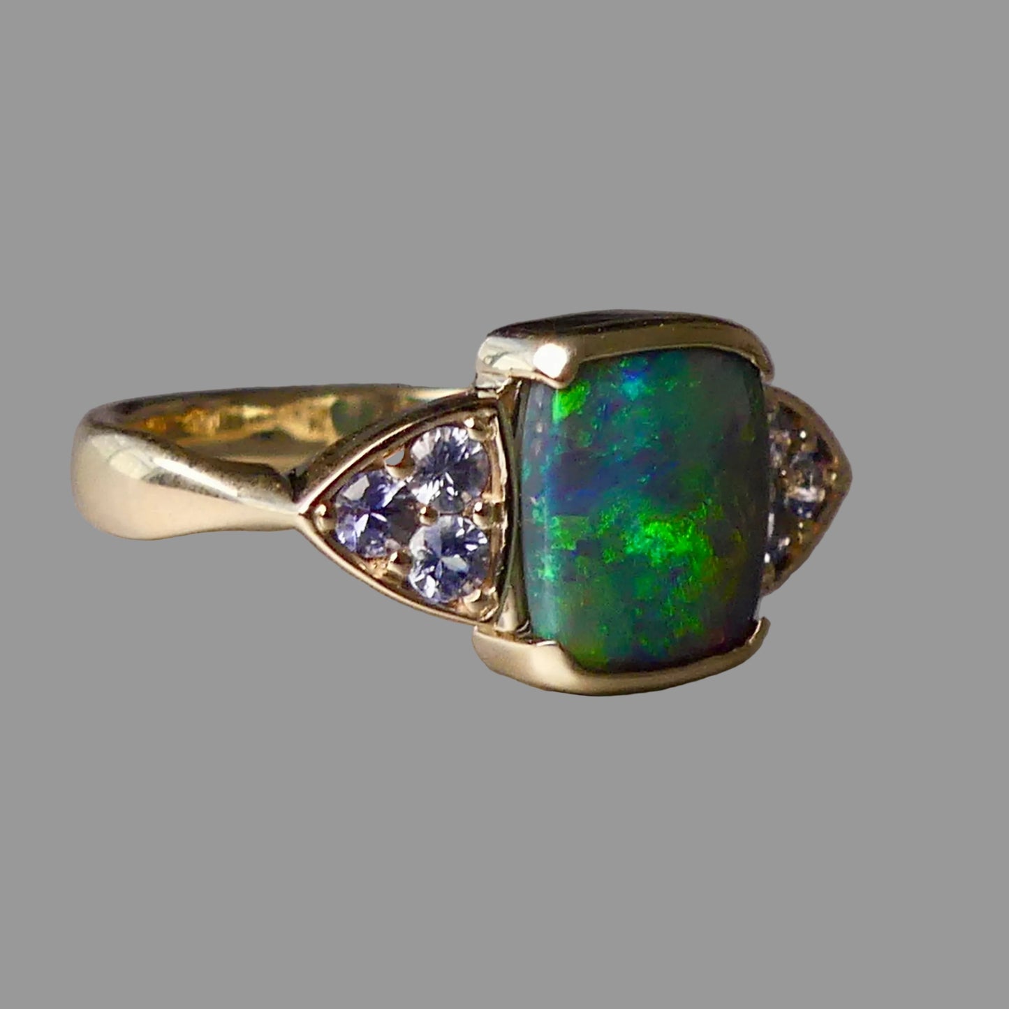 Gold ring with a green opal stone and smaller gemstones on a gray background