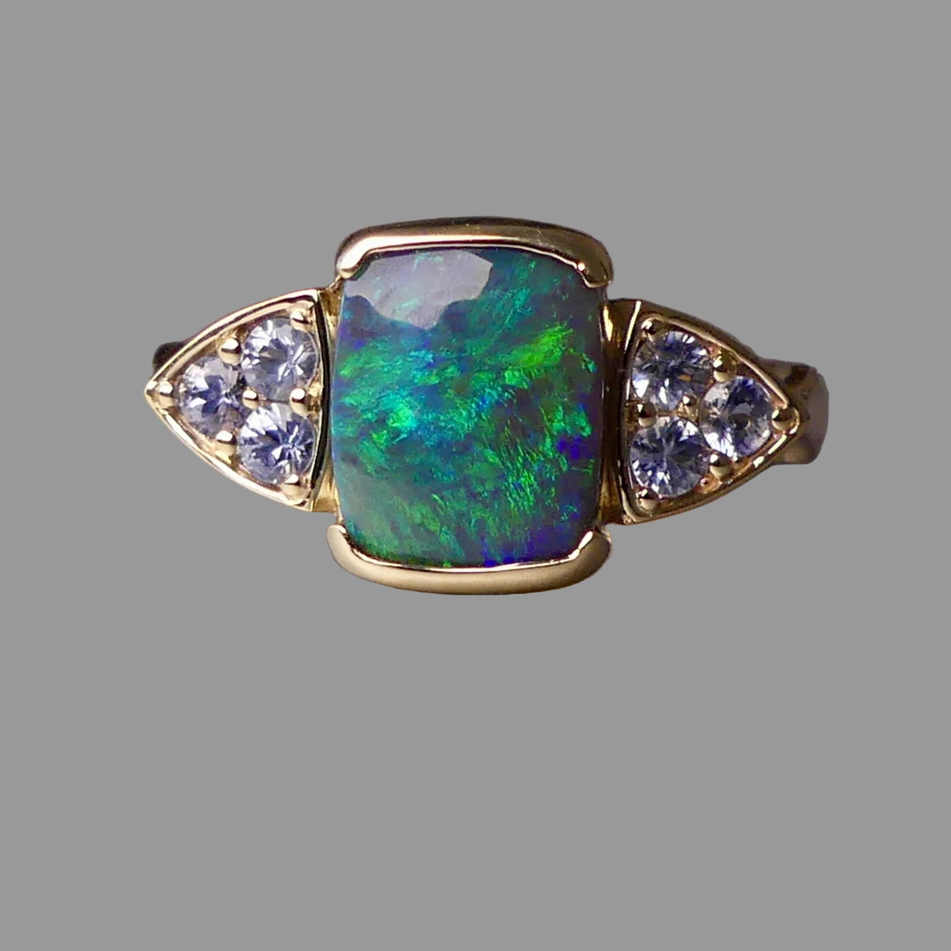 Gold ring with a colorful gemstone and diamond accents on a gray background