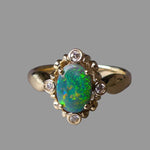 Gold ring with a colorful gemstone and smaller diamonds on a gray background