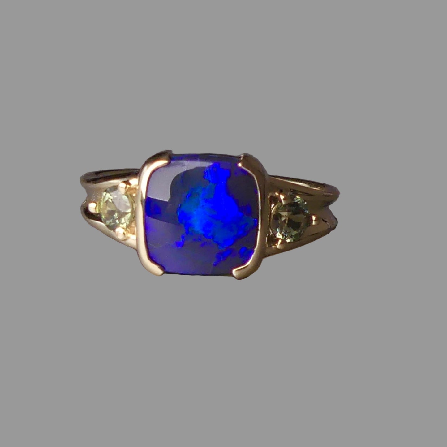 Ring with a blue gemstone and smaller green stones on a gray background