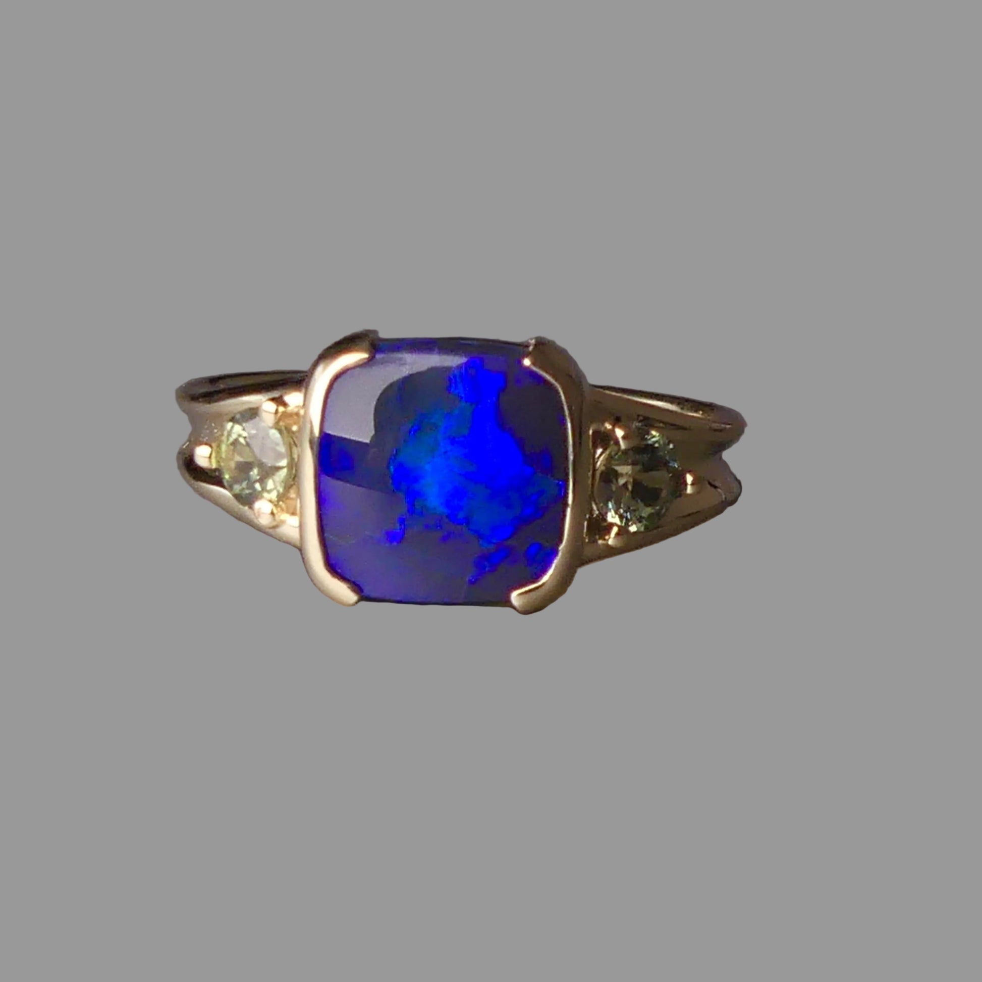 Ring with a blue gemstone and smaller green stones on a gray background
