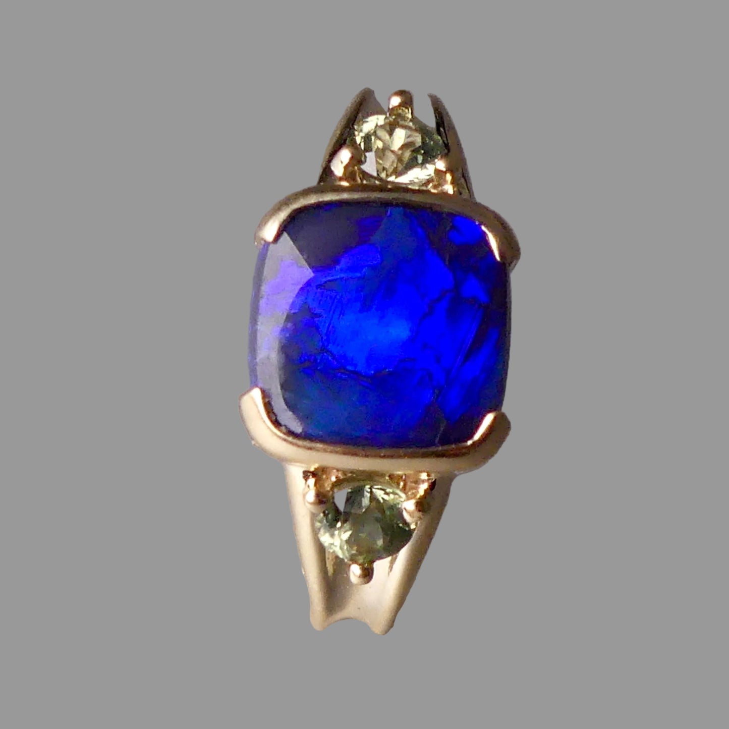 Gold ring with a blue gemstone and smaller green gemstones on a gray background