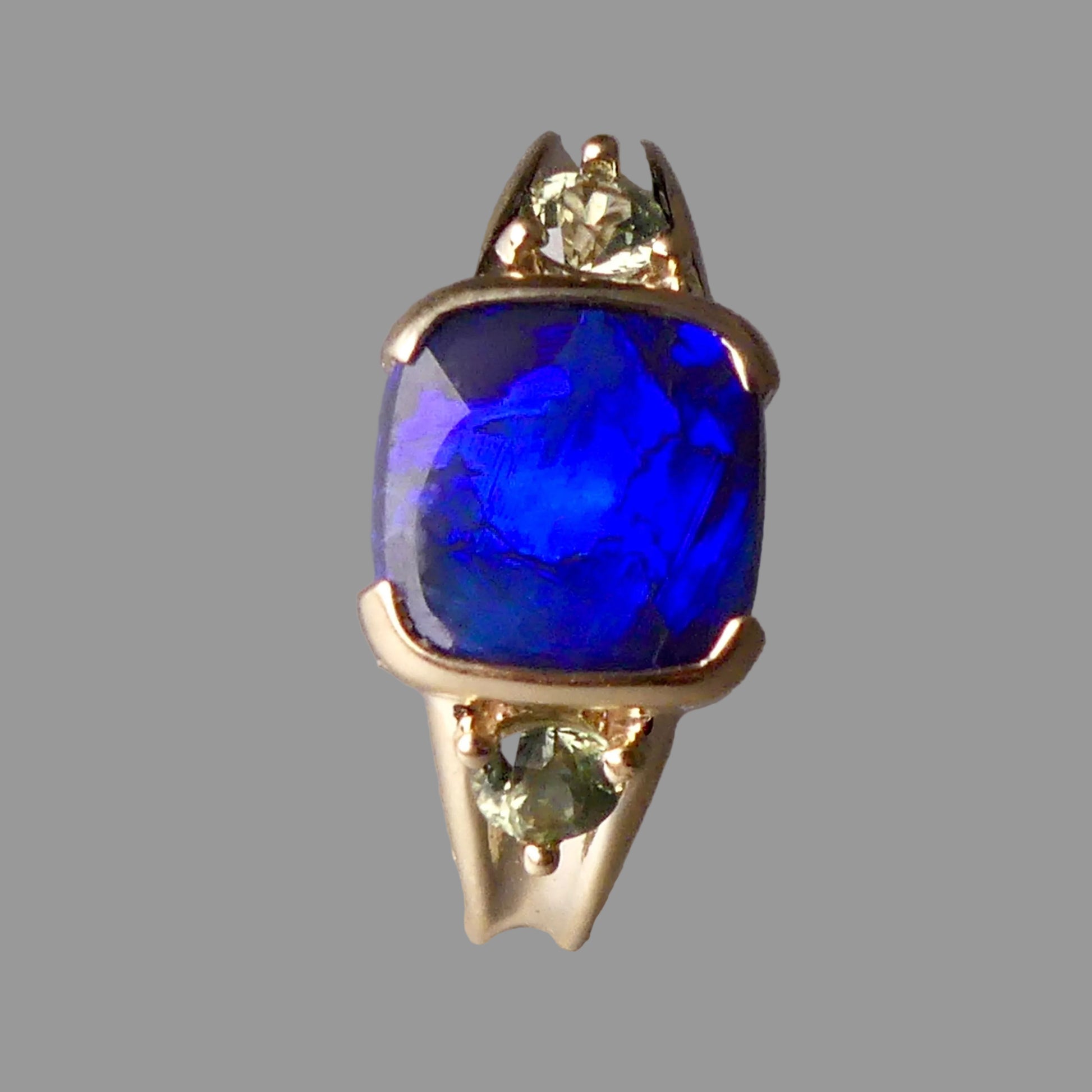 Gold ring with a blue gemstone and smaller green gemstones on a gray background