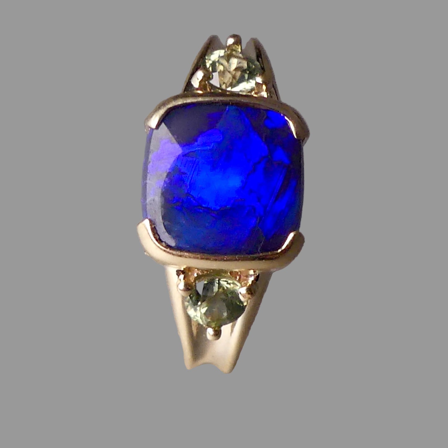 Ring with a blue gemstone and two green gemstones on a gray background
