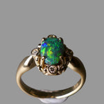 Gold ring with a green gemstone and small diamonds on a dark background